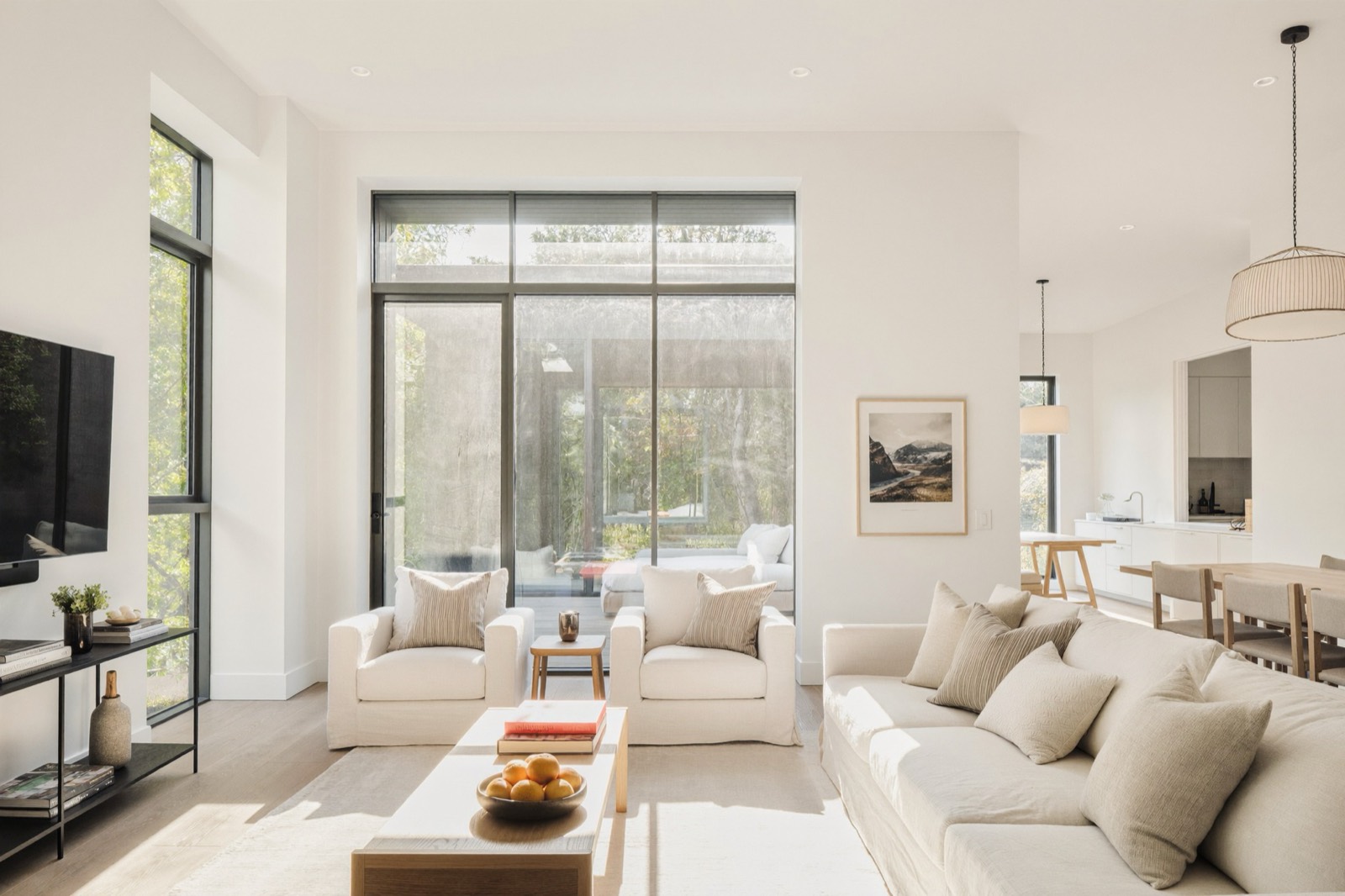 A living room with pale linen sofas, full-height glass onto a deck and a view of trees beyond.