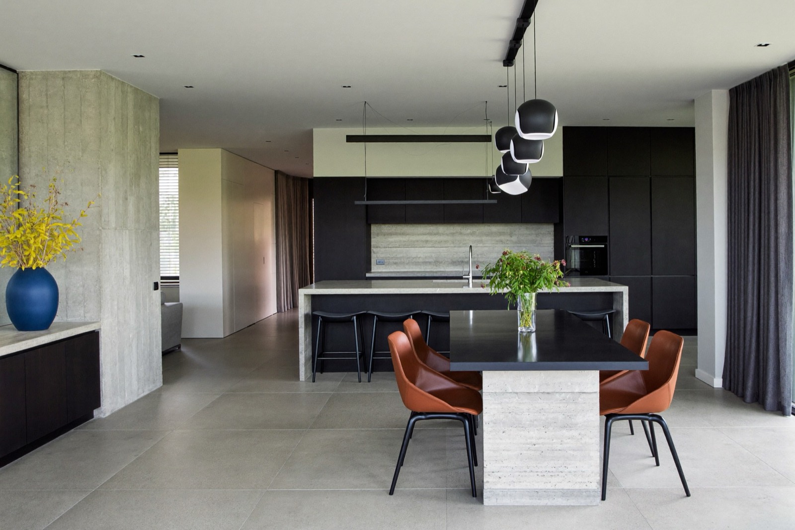An open-plan kitchen in black, concrete and travertine, with an amber corner mark and a disclosure label.